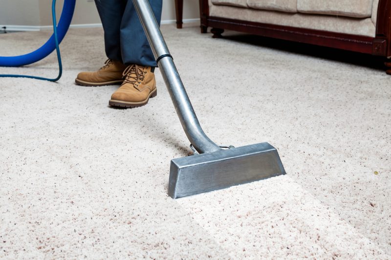 A technician running a carpet cleaning wand over commercial carpet