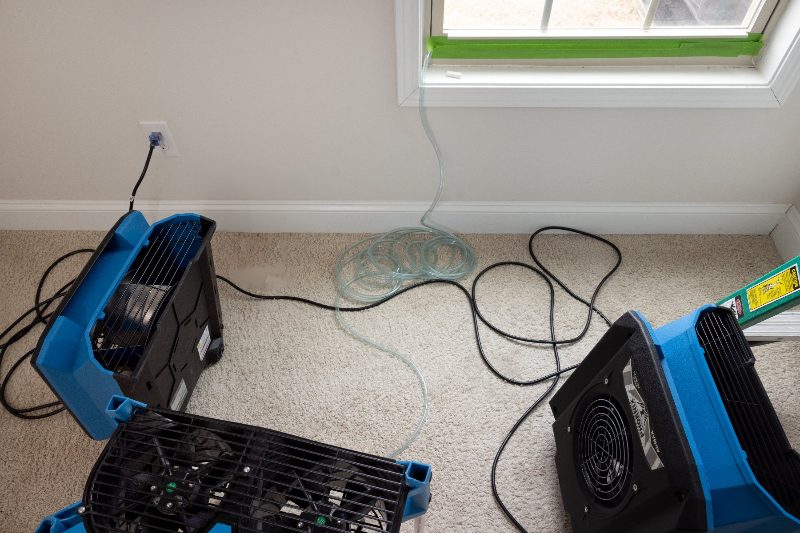 Air movers and a dehumidifier drying a room after water damage